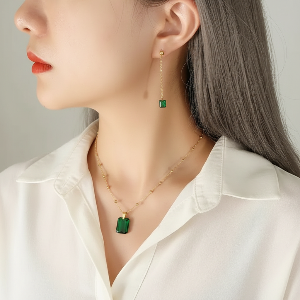 Close-up of a person wearing gold earrings and necklace with green emerald on a neutral background