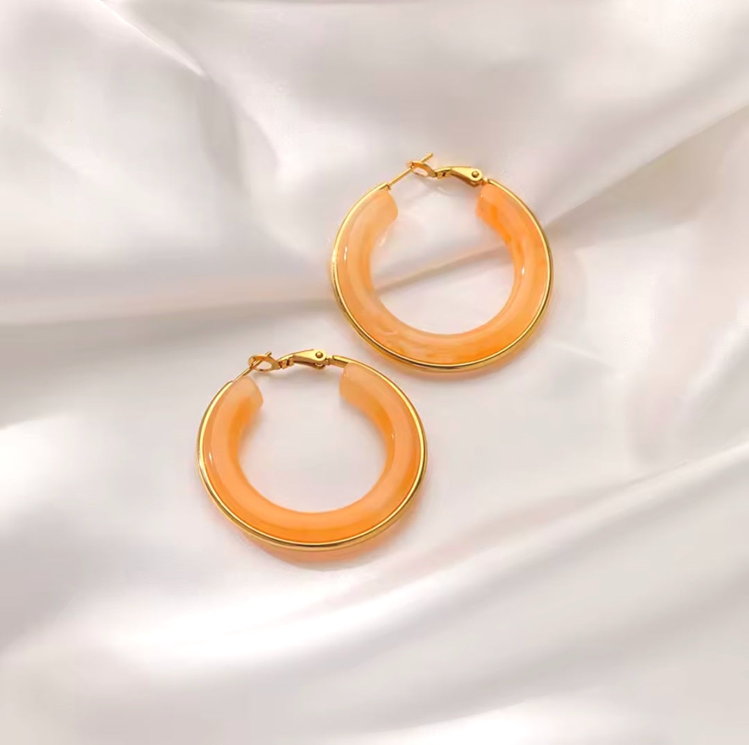 TISA Lera Hoop Earrings - 18k gold-plated, orange-colored hoop earrings made of resin, displayed against a white background