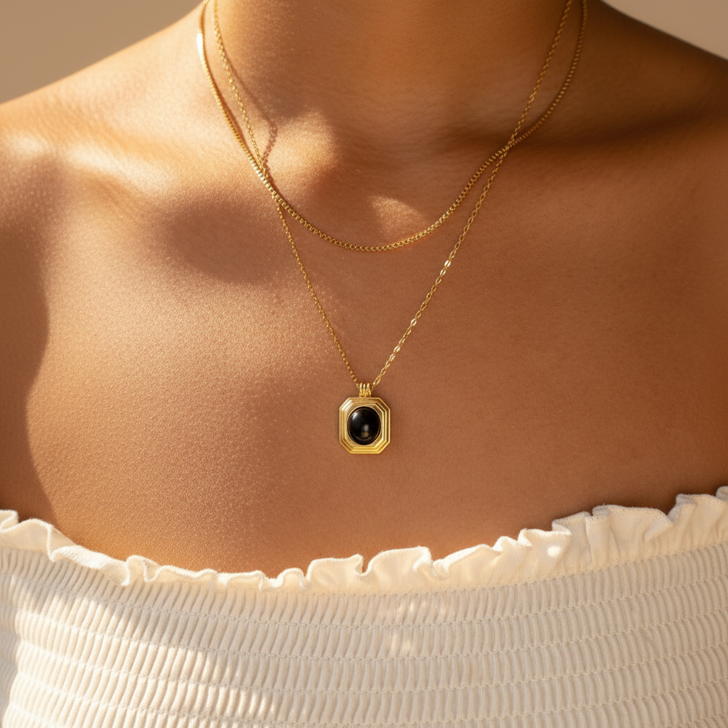 Gold necklace with a black pendant on a person wearing a white top.