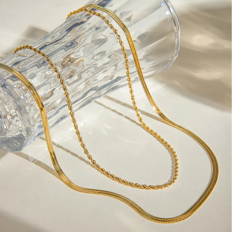 18k gold plated dual chain necklace on a light surface with a clear glass object