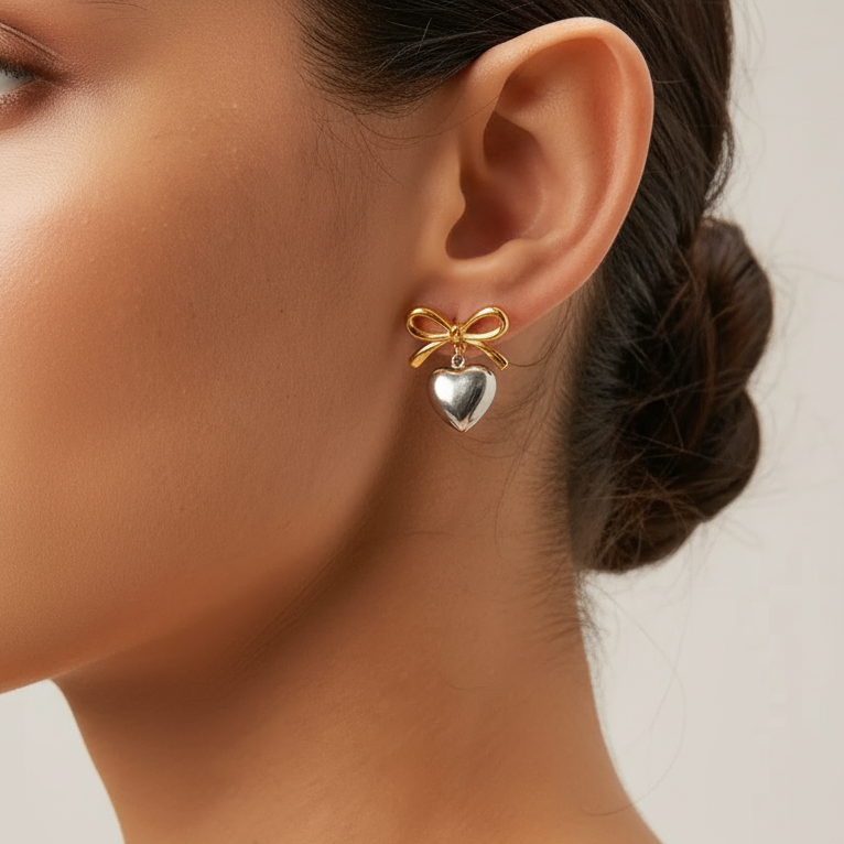 Tisa 18k Gold plated bow-shaped Belle dual-tone earring with a heart charm worn by a model.