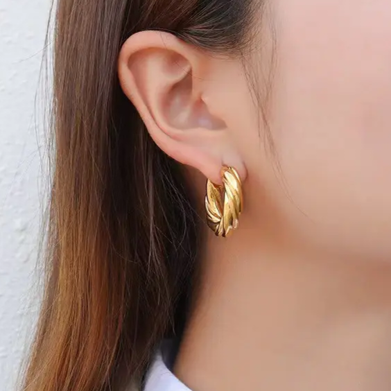A close-up of a person's ear wearing a textured Braided Croissant Hoop earring against a light neutral background.
