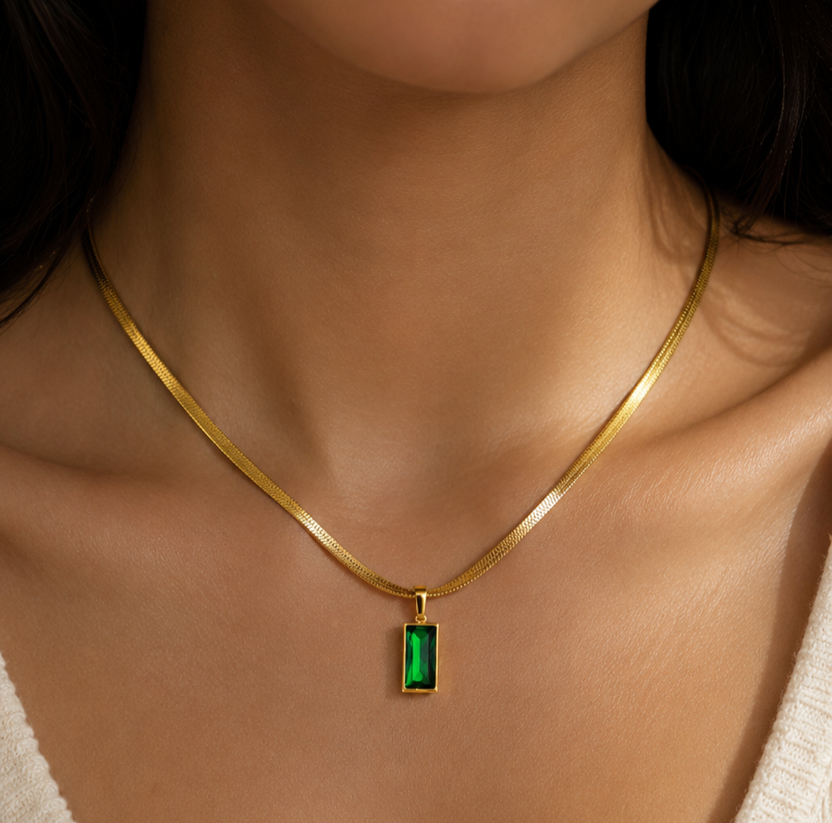 A model wearing Tisa Emerald Luxe Pendant Necklace featuring a  snake chain with a green emerald gemstone.