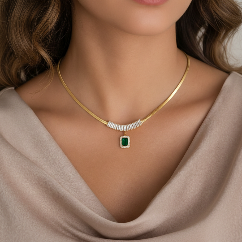 A model wearing a beige outfit wearing Tisa 18k gold platedEmerald Radiance Pendant Necklace featuring a snake chain with baguette zircons with a centered emerald pendant.