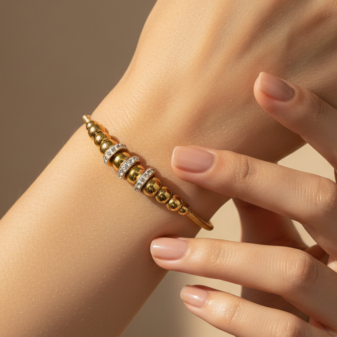 Tisa's 18k Gold plates bracelet with beads and zircons on a wrist against a neutral background.