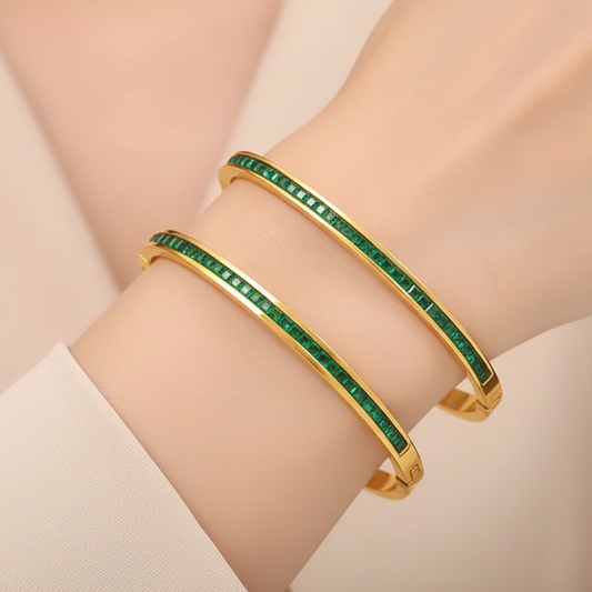 Model wearing Tisa 18k pvd gold platedal bangles with green gemstones on a wrist against a neutral background.
