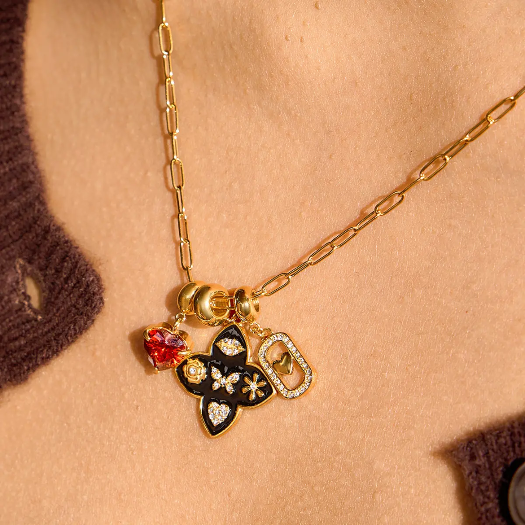 A 18k Gold plated necklace with a butterfly clover charm and heart charms on a person's neck