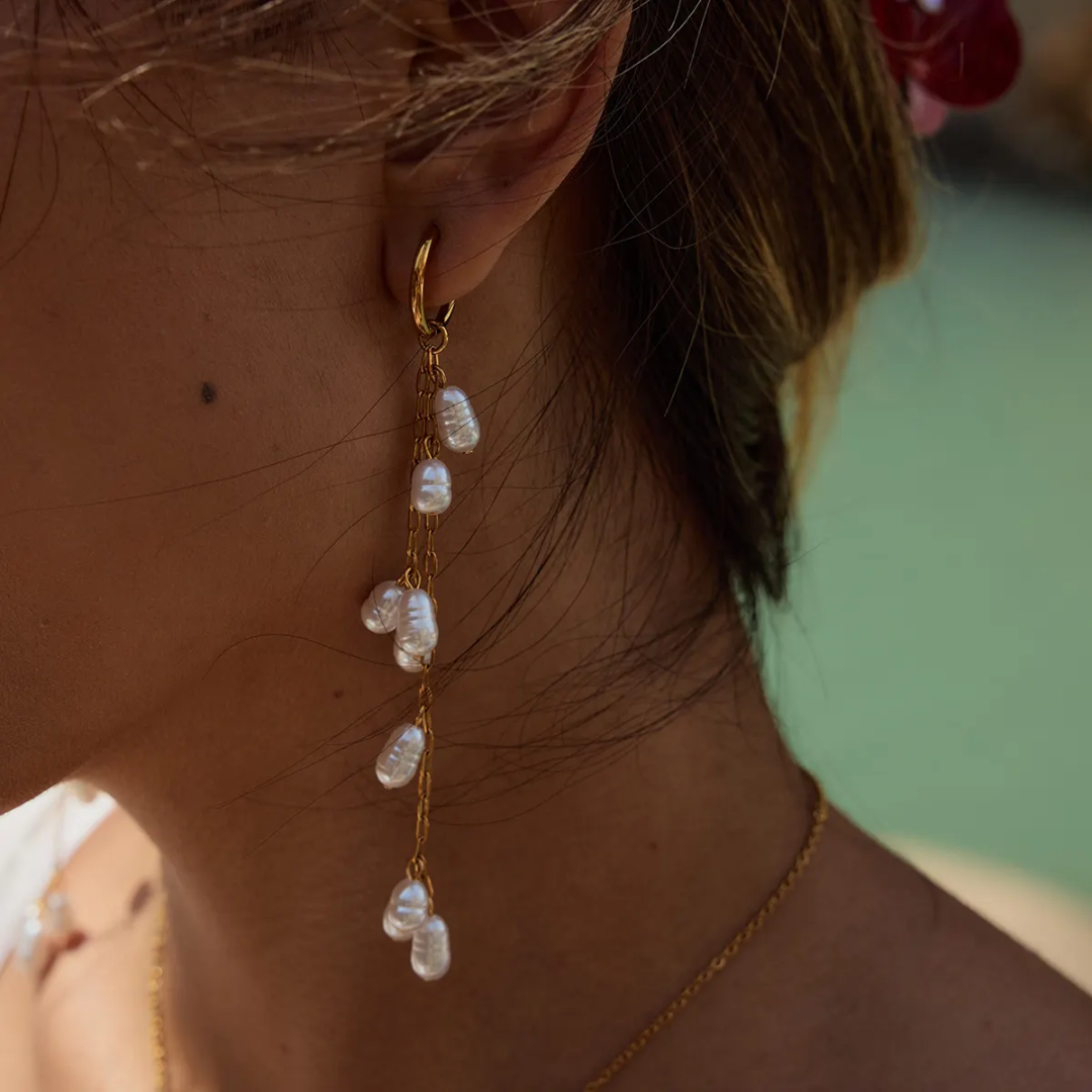 Close-up of a woman wearing Tisa 18K gold plated earrings with pearl-like stones against a blurred background.