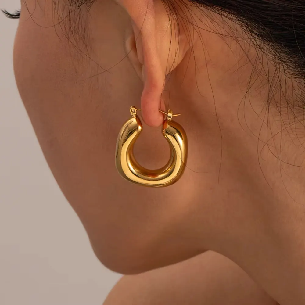 A close-up of a person's ear wearing Tisa 18k gold plates thick, polished hoop earring.