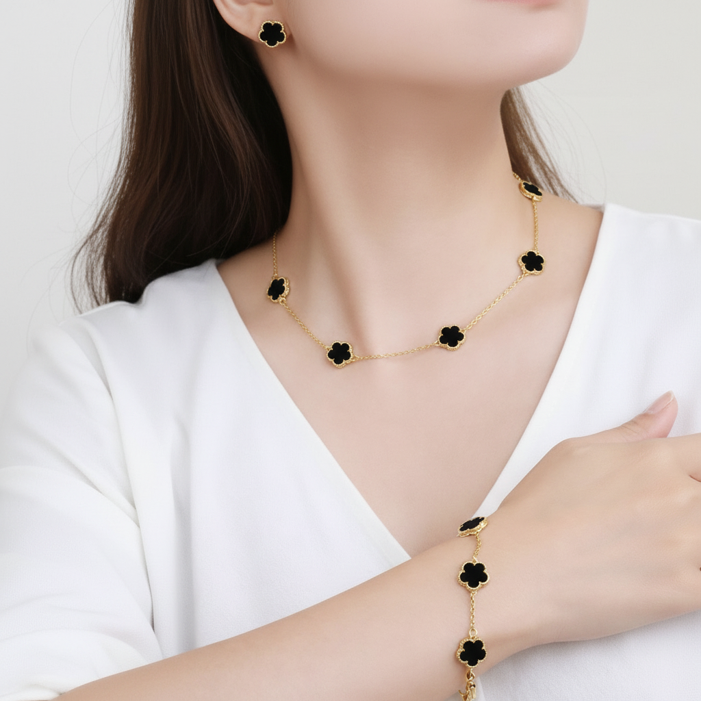 Woman wearing a 18k gold plated clover necklace, earring and bracelet with black flower accents on a white background