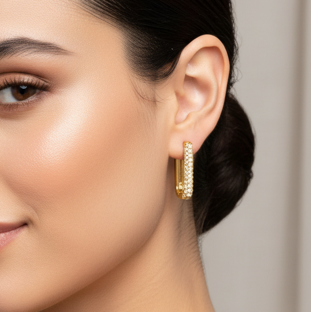 Close-up of a woman wearing tisa 18k gold plated hoop earrings with a neutral background