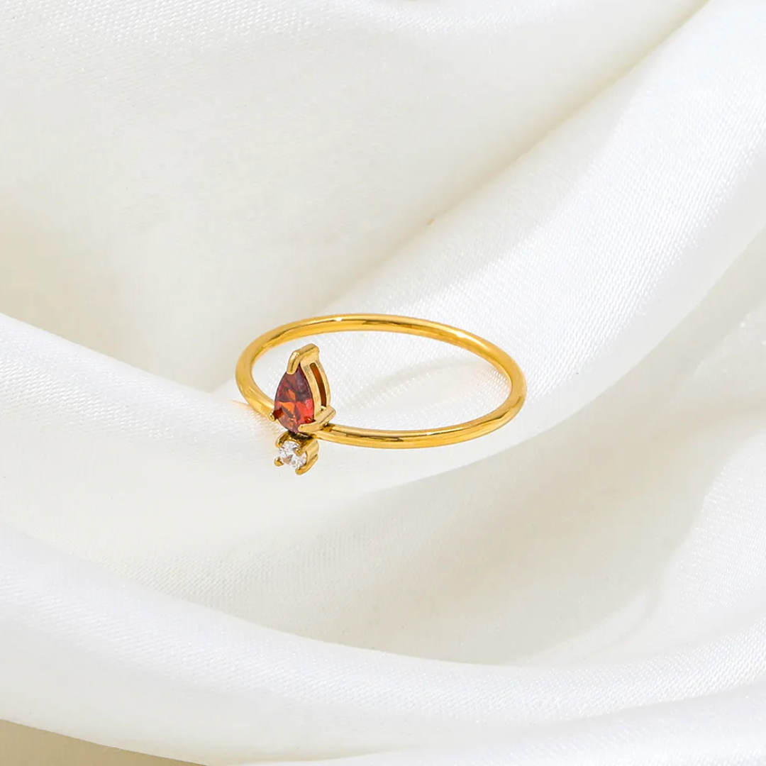 Tisa 18k Gold plated ring with a red garnet gemstone on a white fabric background.