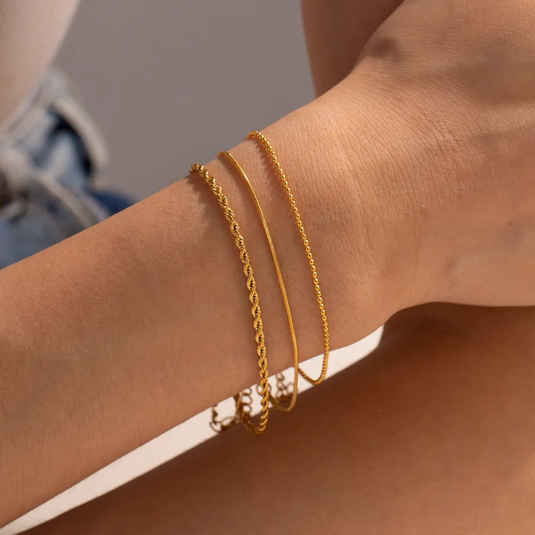 Tisa 18k Gold plated trio chain bracelet set on a model's wrist with a neutral background. 