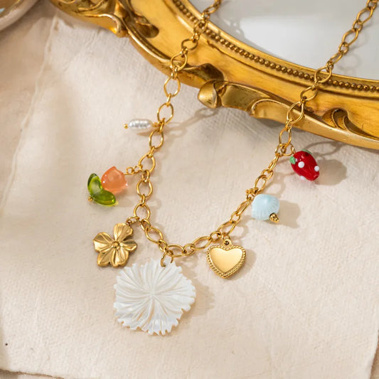 Tisa 18k gold-plated necklace with various charms on a beige fabric background