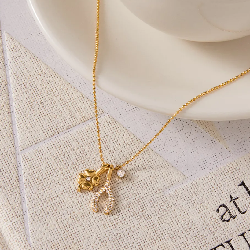 18k Gold-plated necklace with charms on a textured surface next to a white coffee cup.